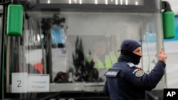 FILE - A Romanian gendarme gestures next to a bus transporting refugees at the Romanian-Ukrainian border, in Siret, Romania, March 5, 2022.