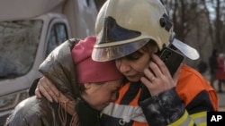 基辅一座居民楼遭轰炸被毁后，消防队员在楼外安慰一名女子。(2022年3月15日)