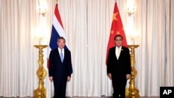 In this photo released by Government Spokesman Office, Chinese Foreign Minister Wang Yi, left, pose for a picture with Thai Prime Minister Prayuth Chan-ocha prior to a meeting at the Government House in Bangkok, Thailand, Thursday, Oct. 15, 2020.