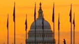 An early morning pedestrian is silhouetted against sunrise as he walks through the US flags on the National Mall and past the US Capitol Building in Washington, Nov. 7, 2022.