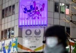 Seorang perempuan mengenakan masker berjalan di dekat spanduk promosi Olimpiade yang dijadwalkan ulang untuk diadakan pada musim panas ini, di Tokyo, Kamis, 28 Januari 2021. (Foto AP / Hiro Komae)