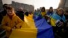 Sejumlah pengunjuk rasa membawa bendera nasional Ukraina saat melakukan protes menentang perang Rusia di Ukraina, menandai peringatan pertama agresi skala penuh Rusia, di Bukares, Rumania, 24 Februari 2023. (Foto: Andreea Alexandru/AP)