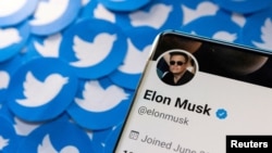 Foto ilustrasi yang menunjukkan akun Twitter Elon Musk yang tersemat pada sebuah layar telepon dengan kumpulan cetakan logo twitter di belakangnya. Foto diambil pada 28 April 2022. (Foto: Reuters/Dado Ruvic)