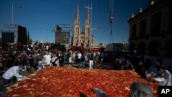 Para juru masak tampak mempersiapkan versi besar "milanesa," roti tradisional yang dicampur dengan daging, dalam perayaan di Lujan, Argentina, pada 3 Mei 2022. (Foto: AP/Victor R. Caivano)