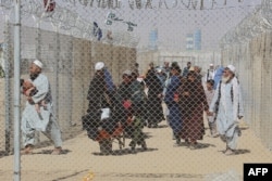 FILE - Afghan people walk inside a fenced corridor as they enter Pakistan at the Pakistan-Afghanistan border crossing point in Chaman, Aug. 25, 2021.