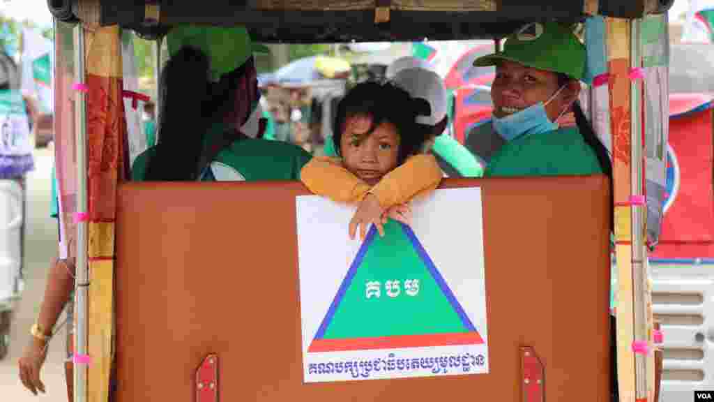 កូនស្រីរបស់អ្នកគាំទ្រគណបក្សប្រជាធិបតេយ្យមូលដ្ឋាន ជិះកង់បីជា​មួយ​ម្តាយ ដើម្បីឃោសនាគោលនយោបាយបក្ស នៅក្នុងសង្កាត់កោះដាច់ ខណ្ឌជ្រោយចង្វារ នៅថ្ងៃទី​២១ ខែឧសភា ឆ្នាំ២០២២។ (លាស់ លីបលីប/វីអូអេ)