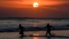 Dua orang tampak berkejar-kejaran di laut saat matahari terbenam di Pantai Mesari, Seminyak, Bali pada 21 Juni 2022. (Foto: AFP/Sonny Tumbelaka)