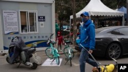 Seorang pria berjalan-jalan dengan anjingnya melewati tempat tes COVID di Beijing, Jumat, 2 Desember 2022. Lebih banyak kota melonggarkan pembatasan, memungkinkan pusat perbelanjaan, supermarket, dan bisnis lain dibuka kembali menyusul protes akhir pekan lalu.(AP/Ng Han Guan)