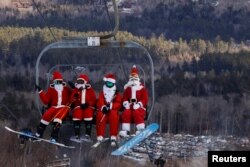 Para pemain ski berpakaian Sinterklas menaiki lift untuk berpartisipasi dalam acara amal di resor ski Sunday River di Bethel, Maine, AS, 5 Desember 2021. REUTERS/Brian Snyder