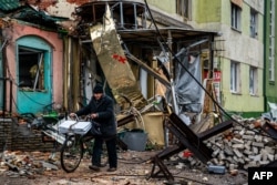 FILE - A local resident pushes his bicycle past "hedgehog" tank traps and rubble, down a street in Bakhmut, Donetsk region, Jan. 6, 2023.