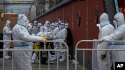Workers in protective suits stand guard at a barricade as others prepare for their duties in a locked-down neighborhood as part of COVID-19 controls in Beijing, Nov. 24, 2022.