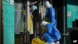 Workers in protective gear prepare to collect COVID samples from a woman at her locked down store in Beijing, Dec. 1, 2022. 