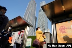 Warga memakai masker menunggu di halte bus dekat gedung pencakar langit di Central Business District di Beijing, Senin, 24 Oktober 2022. (Foto: AP)