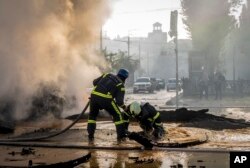 Seorang petugas pemadam kebakaran membantu rekannya melarikan diri dari kawah setelah serangan Rusia di Kyiv, Ukraina, 10 Oktober 2022. (Foto: AP)