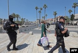 Anggota polisi perbatasan Israel mengawal seorang perempuan Israel di dekat Gerbang Damaskus di Kota Tua Yerusalem, di tengah langkah-langkah keamanan yang meningkat, 15 April 2022. Lebih dari 100 orang terluka dalam kekerasan baru, yang terjadi setelah tiga minggu ketegangan akibat kekerasan di Israel dan Tepi Barat bersamaan dengan perayaan Passover warga Yahudi, Paskah umat Kristiani dan bulan suci Ramadan umat Muslim. (Foto: GIL COHEN-MAGEN / AFP)