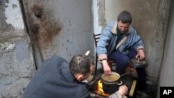 Penduduk Mariupol memasak sambil duduk di pintu masuk gedung apartemen mereka yang rusak di daerah yang diklaim dikuasai oleh separatis dukungan Rusia di kota Mariupol, Ukraina, Rabu, 13 April 2022. (AP Photo/Alexei Alexandrov)