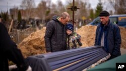 Vova, 10, looks at the coffin carrying body of his mother, Maryna, as his father, Ivan Drahun, hugs him during her funeral in Bucha, on the outskirts of Kyiv, April 20, 2022.