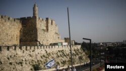Beberapa pemuda membawa bendera Israel saat berjalan di dekat tembok yang mengelilingi Kota Tua Yerusalem, dalam pawai menandai Hari Yerusalem, di tengah ketegangan Israel-Palestina, 10 Mei 2021. (REUTERS/Nir Elias)