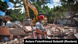 Seorang pria membawa foto Presiden Joko Widodo dari sekolah yang rusak akibat gempa di Gunungsari, Lombok, 12 Agustus 2018.