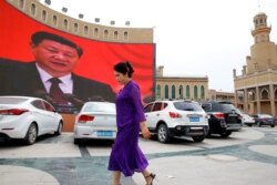An ethnic Uyghur woman walks in front of a giant screen with a picture of Chinese President Xi Jinping in the main city square in Kashgar on September 6, 2018. (Thomas Peter/Reuters)