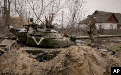 Seorang prajurit Ukraina berjalan di atas tank tentara Rusia yang ditinggalkan di Andriivka, Ukraina, Selasa, 5 April 2022. (Foto: AP)