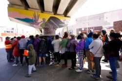 FILE - People surround a car as it arrives carrying food donations at a makeshift camp for migrants seeking asylum in the United States at the border crossing in Tijuana, Mexico, March 12, 2021.