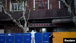 FILE - A person in a protective suit looks over barricades set around a sealed-off area, during a lockdown to curb the spread of the coronavirus disease (COVID-19) in Shanghai, China, April 11, 2022.
