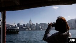 Seorang perempuan mengambil foto dari atas kapal feri di Hong Kong, 2 Februari 2023. Hong Kong menawarkan penerbangan gratis dan voucer untuk merayu wisatawan dalam upaya mengatasi persaingan regional yang sengit. (ISAAC LAWRENCE / AFP)