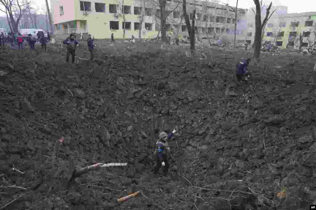 Ukrainian soldiers and emergency employees checks the bomb crater outside a severely damaged maternity hospital by a Russian air strike in the besieged port city of Mariupol, Ukraine, March 9, 2022.