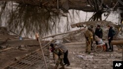 Seorang tentara Ukraina menggendong seorang perempuan lansia saat hendak menyeberangi sungai Irpin di pinggiran Kyiv, Ukraina, Senin, 7 Maret 2022. (AP/Emilio Morenatti)