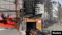 Sejumlah warga sedang makan di luar sebuah gedung yang rusak akibat serangan oleh Rusia ke Ukraina di kota pelabuhan, Mariupol, Kamis, 31 Maret 2022. (Foto: Alexander Ermochenko/Reuters)