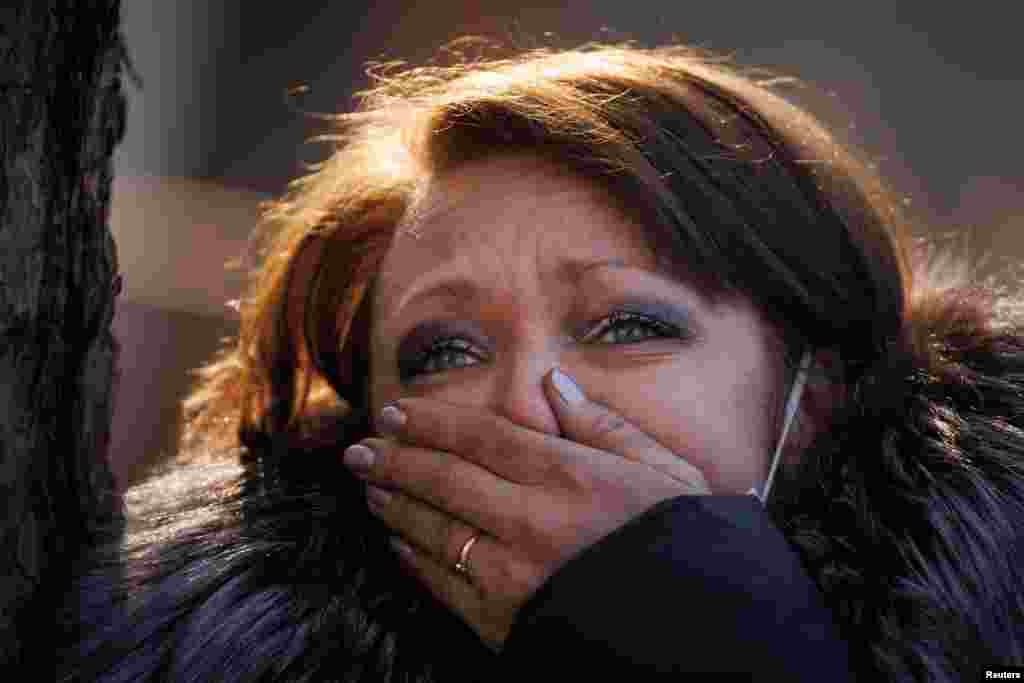 A resident watches rescue efforts outside her apartment building that was hit by a shell in Kyiv, March 15, 2022.