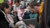 A woman holds a child as a humanitarian aid worker checks the identities of refugees boarding a bus bound for Portugal outside the main shelter and relocation center in Przemysl, southeastern Poland on March 16, 2022.