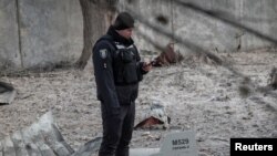 在基辅一处被俄罗斯无人机破坏的建筑附近，一名警察站在无人机残骸边。(2022年12月14日)