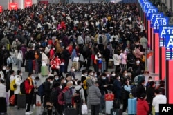 “春运”在如同海啸般蔓延的新冠感染爆发中拉开帷幕。广东深圳南站大厅内，旅客们人们带着口罩和行李，熙熙攘攘挤满大厅，等待买票和登车。本照片由新华社发布，美联社提供。