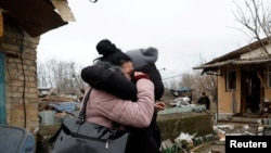 在基辅，一名当地居民在被俄罗斯导弹袭击破坏的房屋与朋友拥抱。(2022年12月29日)