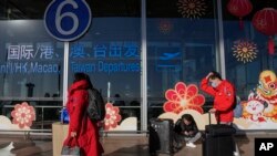 旅客戴着口罩拖着行李来到北京首都机场国际航班出发航站楼入口（2022年12月29日）