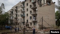 Sejumlah warga lokal mengamati gedung perumahan warga yang hancur akibat serangan pasukan Rusia di Kota Chasiv Yar, wilayah Donetsk, Ukraina, pada 11 Juli 2022. (Foto: Reuters/Gleb Garanich)