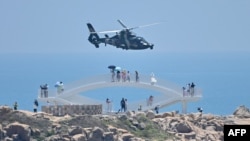 Turis mengamati helikopter militer China terbang melewati pulau Pingtan, salah satu titik terdekat daratan China dari Taiwan, di provinsi Fujian, 4 Agustus 2022, menjelang latihan militer besar-besaran di Taiwan setelah kunjungan Ketua DPR AS Nancy Pelosi, (Hector RETAMAL / AFP)