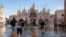 FILE - People cross St Mark's Square flooded by sea tide, in Venice, Italy, Dec. 4, 2021. The water reached 99 centimeters above sea level and the lowest parts of town went underwater.