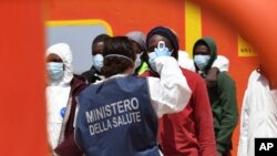 FILE - An Italian health worker takes the temperature of migrants disembarking from a rescue ship on the island of Lampedusa, Italy, May 11, 2021. A new report has found that refugees and migrants have insufficient access to health services in their host countries.