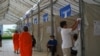Buddhist monks walk pass a polling station as a man reviews a voter list ahead of commune election day, in Phnom Penh, on Saturday, June 4, 2022. (Khan Sokummono/VOA Khmer)