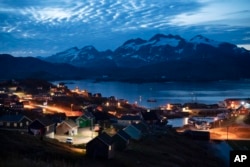FILE - Homes are illuminated after sunset in Tasiilaq, Greenland, Aug. 16, 2019. Greenland has been controlled by Denmark for centuries, though its 57,000 people now govern their own domestic affairs.