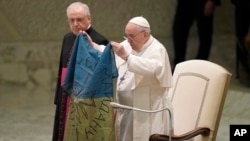 Pope Francis shows a flag that he said was brought to him from Bucha, Ukraine, during his weekly general audience in the Paul VI Hall, at the Vatican, Wednesday, April 6, 2022. (AP Photo/Alessandra Tarantino)