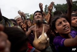 Seorang pria Rohingya mengulurkan tangannya untuk meminta makanan yang dibagikan oleh relawan setempat, dengan sekantong beras yang dimasukkan ke dalam singletnya di Kutupalong, Bangladesh. (Foto: AP)