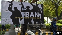 Personel Pasukan Aksi Cepat (RAF) berjaga di samping spanduk yang dipasang oleh para pendukung dan aktivis Partai Bharatiya Janata (BJP) yang berkuasa di India selama protes menuntut larangan organisasi Front Populer India (PFI) di New Delhi pada 28 Februari 2021 (Foto: AFP)