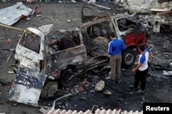Men inspect a wrecked vehicle after explosions hit a bus station in Jableh, in Syria's Latakia province, May 23, 2016.
