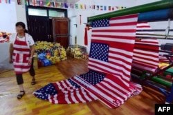 A Chinese employee walks past newly made U.S. flags at a factory in Fuyang in China's eastern Anhui province, July 13, 2018. As the U.S.-China trade war rages, a factory set amid corn and mulberry fields in central China stitches together U.S. and "Trump 2020" flags.
