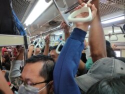 Para penumpang, sebagian besar mengenakan masker, tampak berdesakan di dalam kereta di Jakarta, hari Senin (23/3) di tengah perebakan virus corona.
