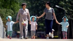 n this June 1, 2017 photo, women walk with children wearing matching hats as they cross a bridge at a public park on International Children's Day in Beijing.